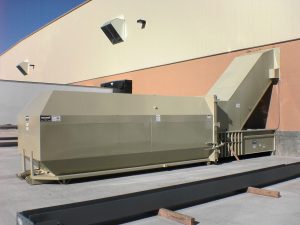 Stationary compactor with a beige finish, positioned outside against a building with pale walls.