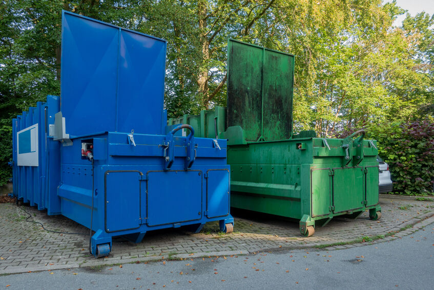 one green and one blue trash compactor in the courtyard of a commercial property 
