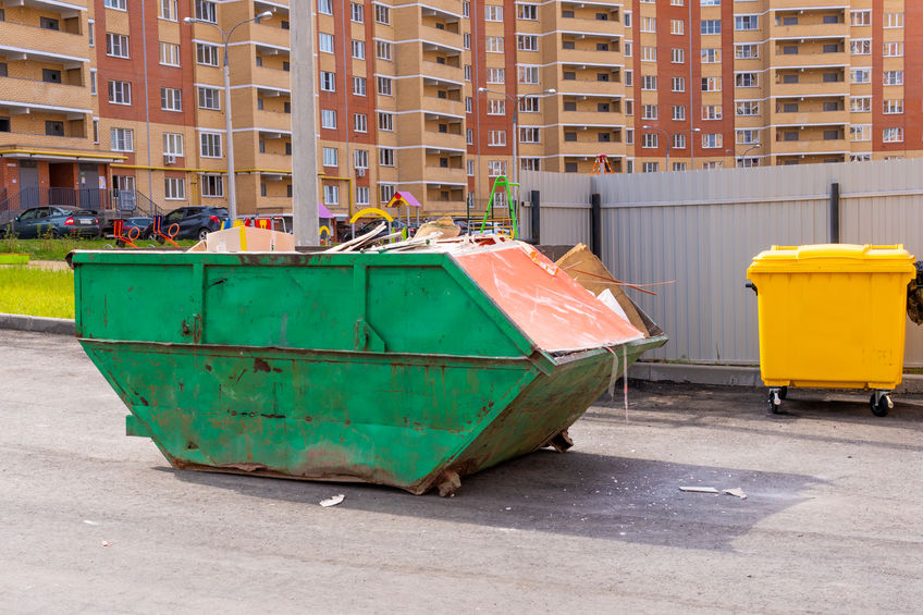 Smelly green dumpster with construction waste in the yard of a multi-story building