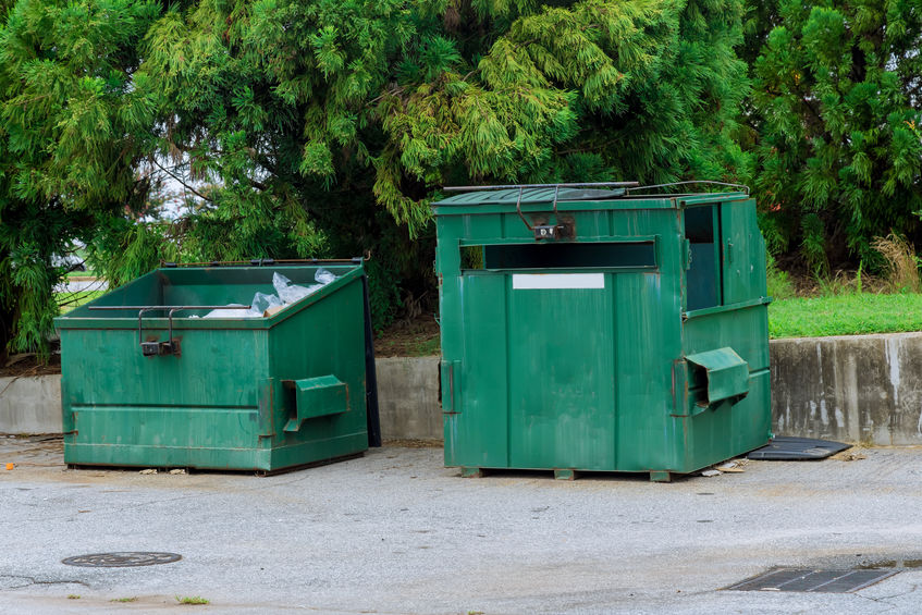 In the vicinity of an commercial building, there is a container bin for garbage