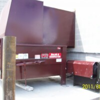 A sizable Stationary Compactor with a red casing is positioned near a concrete wall, with the image dated 2011/08/03.