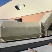 Stationary compactor with a beige finish, positioned outside against a building with pale walls.