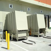 A row of loading dock doors numbered 4 to 7, with two large beige Stationary Compactors in front, and a metal staircase to the left.