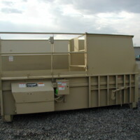 OLYMPUS DIGITAL CAMERA Stationary compactors situated on a gravel lot with a cloudy sky in the background.