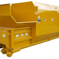 Yellow industrial waste compactor with a large hopper and safety labels, designed for compressing waste materials.