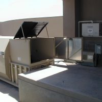 OLYMPUS DIGITAL CAMERA Rooftop industrial HVAC unit with open access panels, situated on a concrete surface near a building wall.