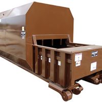 Brown industrial waste compactor with a container on wheels, used for compressing large volumes of waste material.