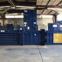 Industrial blue compactor machine in a warehouse setting, surrounded by concrete floor and metal beams.