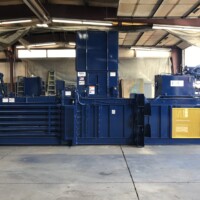 Industrial blue compactor machine in a warehouse setting, surrounded by concrete floor and metal beams.