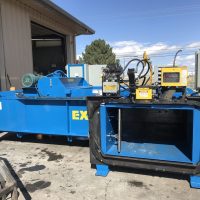 Industrial machinery outside a building; includes a large blue baler with yellow control system.