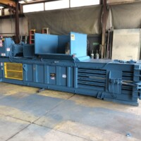 A large blue industrial baler machine in a warehouse setting.