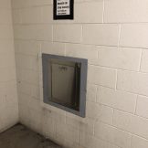 A metal chute on a white brick wall with a sign above that reads, "Please do not put boxes in the chute.
