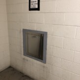 A metal chute on a white brick wall with a sign above that reads, "Please do not put boxes in the chute.