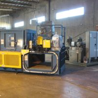 Industrial machinery inside a factory with large metal structures and control panels on a concrete floor.