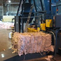 A large machine compresses shredded paper into rectangular bales inside an industrial warehouse setting.