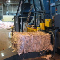A large machine compresses shredded paper into rectangular bales inside an industrial warehouse setting.