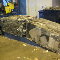 Compacted bundle of crushed metal and cardboard near a baling machine inside an industrial facility.