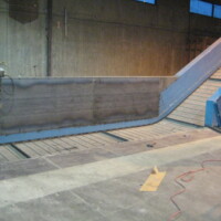 Interior of an industrial facility with a large conveyor system and scattered equipment on the floor.