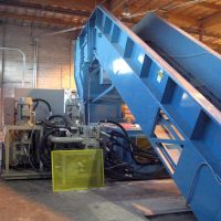 Industrial machine with blue conveyor belt inside a warehouse.