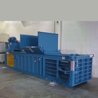 A large blue industrial baler machine inside a warehouse, used for compacting waste materials.