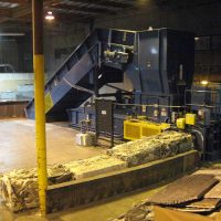 Industrial shredder machine processing debris in a dimly lit warehouse with a person walking in the background.